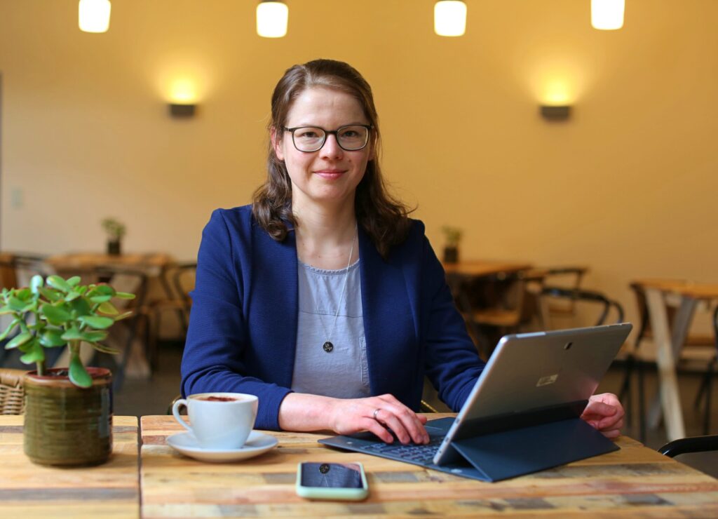 Juliane Becher - Jule, die Content-Macherin sitzt am Laptop und lächelt in die Kamera.