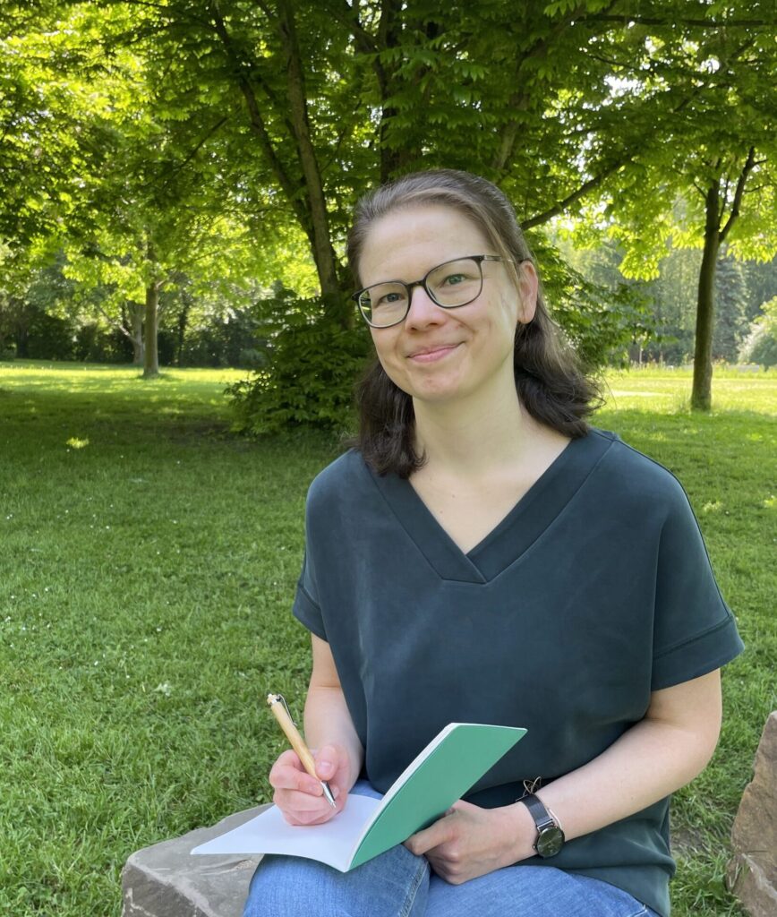 Juliane Becher sitzt in der Natur und schreibt Ideen in ein Notizbuch