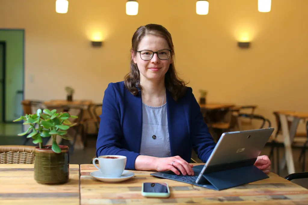 Juliane Becher_Laptop_Handy_Kaffee Juliane Becher - Jule, die Content-Macherin sitzt am Laptop und lächelt in die Kamera.