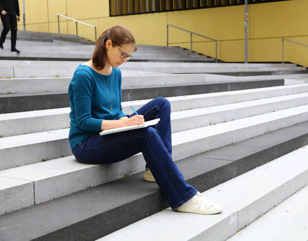 Jule Becher_Steintreppe Juliane Becher sitzt auf einer Steintreppe und schreibt etwas auf ihren Ideenblock.